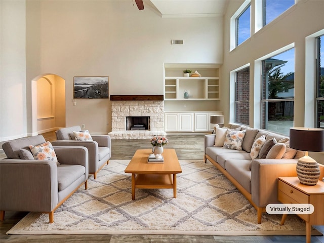 living room featuring arched walkways, a stone fireplace, wood finished floors, a towering ceiling, and visible vents