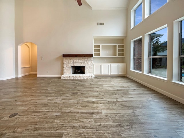 unfurnished living room with arched walkways, visible vents, a towering ceiling, a stone fireplace, and wood finished floors