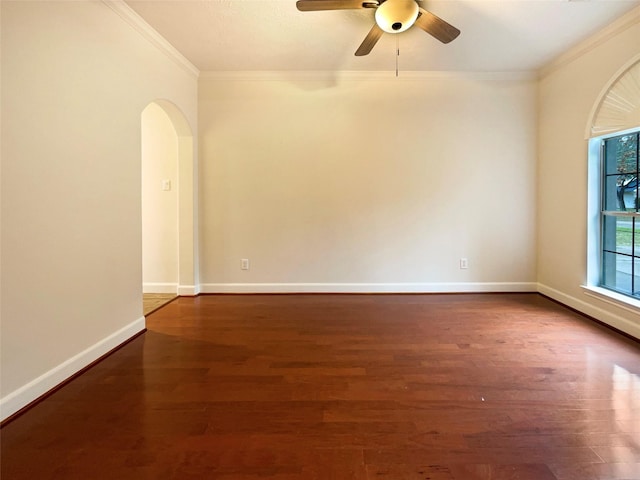 spare room featuring arched walkways, ornamental molding, ceiling fan, wood finished floors, and baseboards