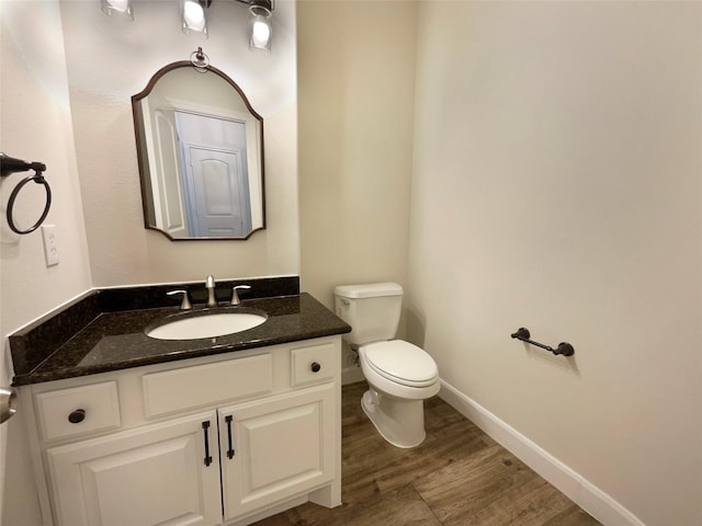 bathroom featuring toilet, baseboards, wood finished floors, and vanity