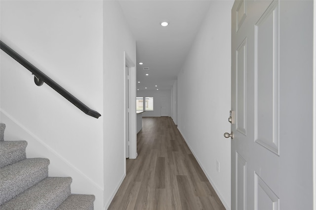 corridor featuring baseboards, stairway, wood finished floors, and recessed lighting