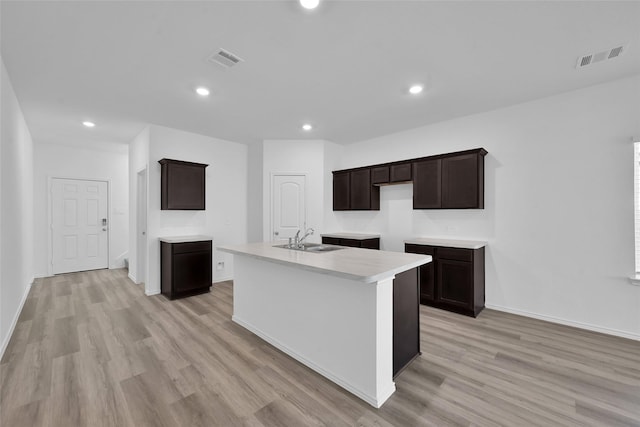 kitchen featuring light wood finished floors, an island with sink, a sink, and visible vents