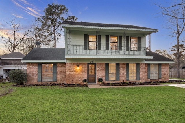 view of front of property featuring brick siding, a lawn, a balcony, and fence