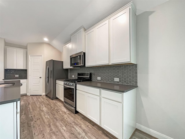 kitchen with dark countertops, light wood finished floors, stainless steel appliances, and backsplash