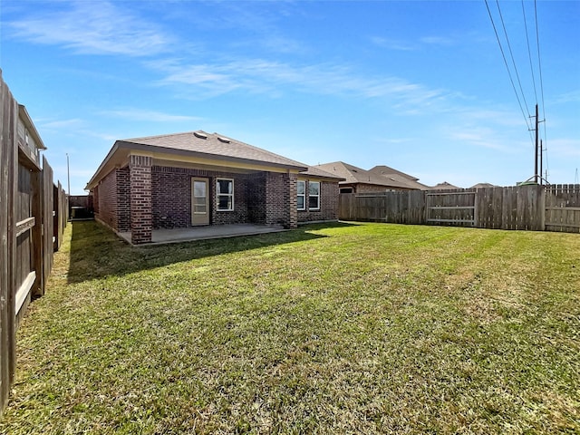 back of property featuring a patio, a fenced backyard, brick siding, a lawn, and roof with shingles