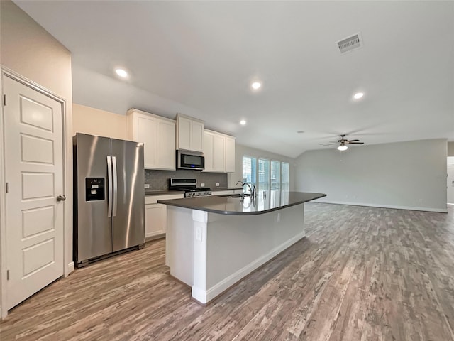 kitchen with stainless steel appliances, light wood-type flooring, dark countertops, and visible vents