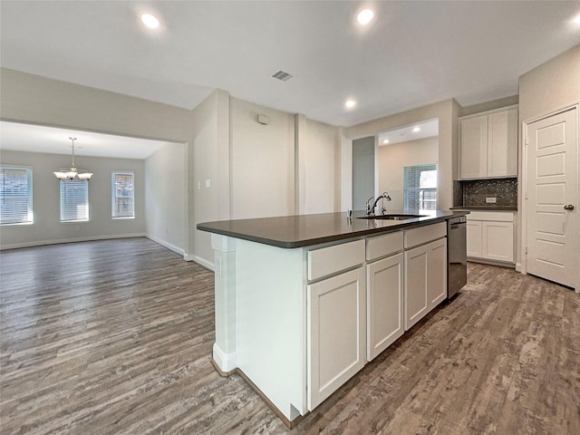 kitchen with a center island with sink, dark countertops, visible vents, a sink, and wood finished floors