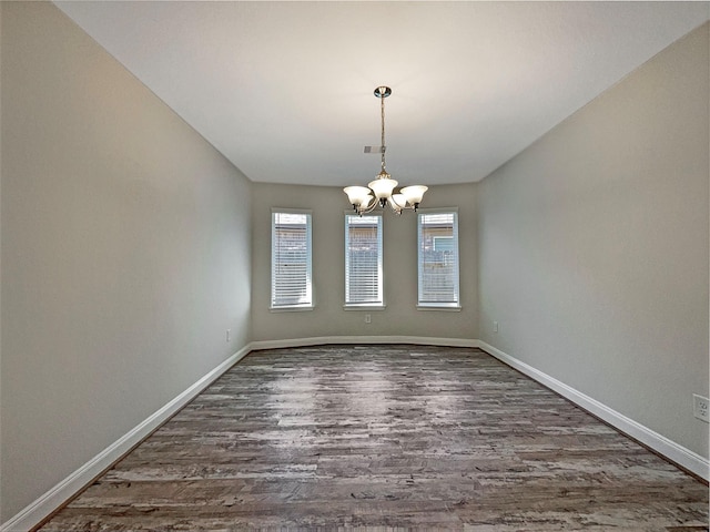 unfurnished room featuring baseboards, wood finished floors, and an inviting chandelier