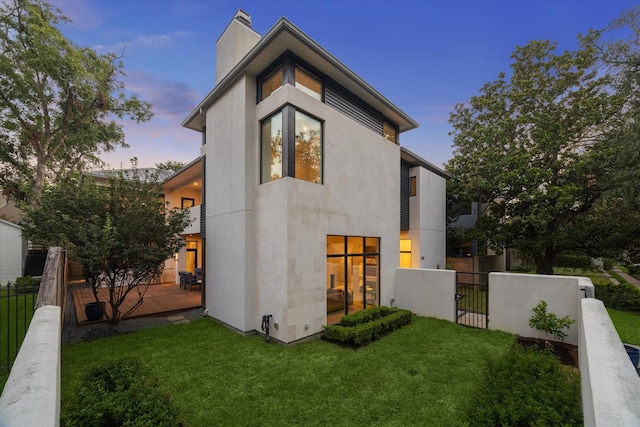 back of property at dusk featuring a yard, a chimney, a gate, fence, and a deck