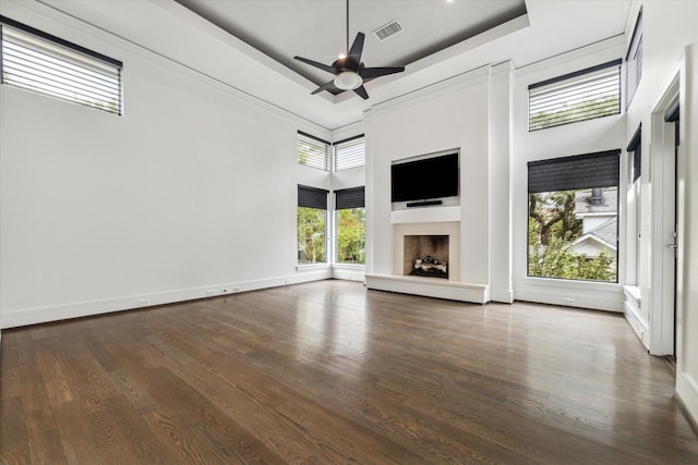 unfurnished living room with visible vents, a tray ceiling, a fireplace with raised hearth, and dark wood-style flooring