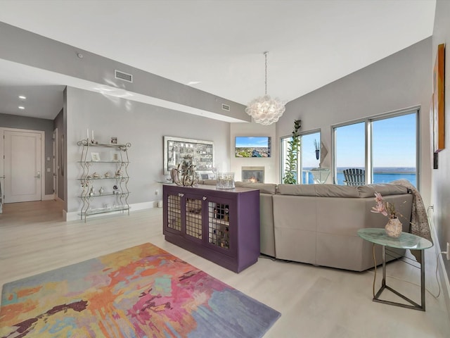 living area featuring a chandelier, wood finished floors, visible vents, baseboards, and a glass covered fireplace