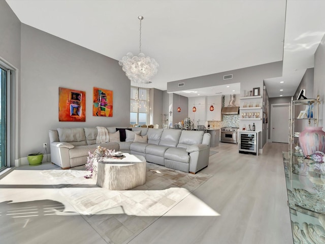 living area featuring a notable chandelier, visible vents, light wood-style flooring, a bar, and beverage cooler