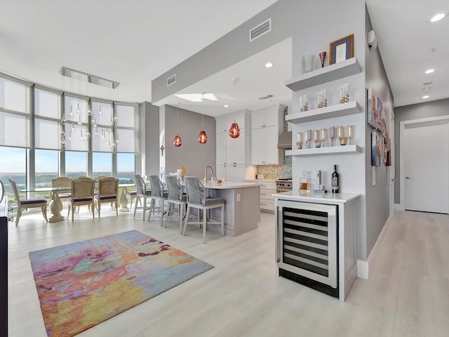 bar featuring tasteful backsplash, visible vents, light wood-style floors, a wall of windows, and beverage cooler