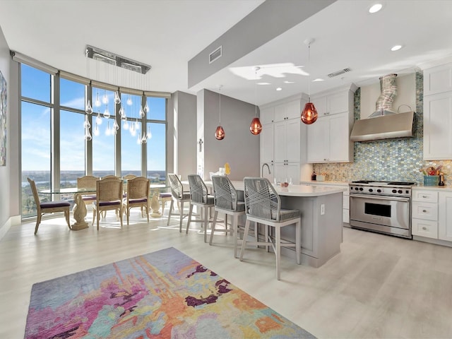 kitchen with luxury range, wall chimney range hood, light wood-type flooring, decorative backsplash, and a wall of windows