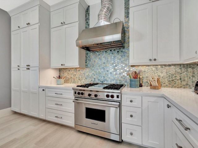 kitchen with designer stove, light countertops, wall chimney range hood, and white cabinets