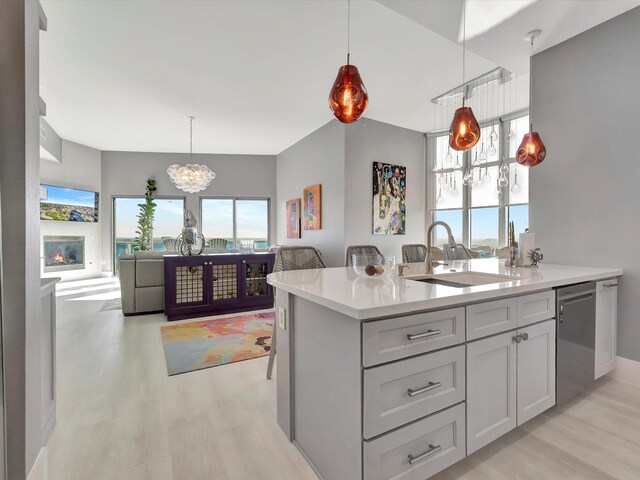 kitchen with light countertops, hanging light fixtures, stainless steel dishwasher, light wood-style floors, and a sink