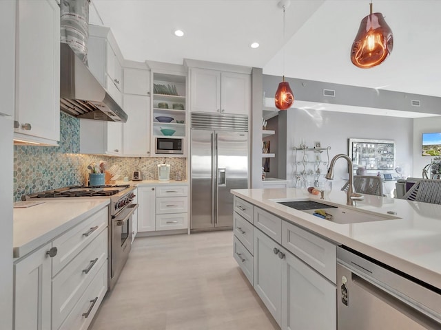 kitchen with light countertops, a sink, wall chimney range hood, and built in appliances