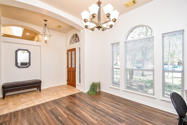 foyer entrance featuring baseboards, visible vents, arched walkways, wood finished floors, and an inviting chandelier