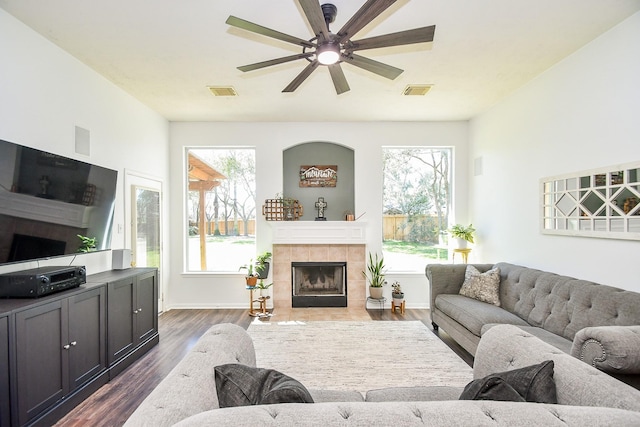 living area with a healthy amount of sunlight, dark wood-style floors, a fireplace, and visible vents