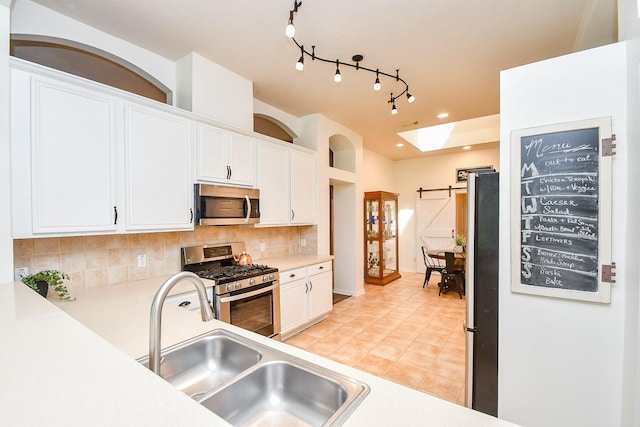 kitchen featuring a barn door, a sink, white cabinetry, appliances with stainless steel finishes, and backsplash