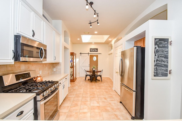 kitchen featuring light tile patterned floors, a barn door, white cabinets, appliances with stainless steel finishes, and tasteful backsplash