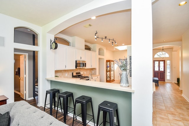 kitchen featuring tasteful backsplash, white cabinets, appliances with stainless steel finishes, a breakfast bar area, and light countertops