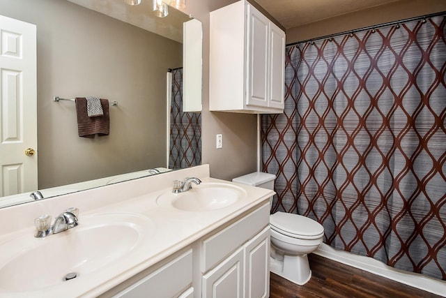 full bath with double vanity, a sink, toilet, and wood finished floors