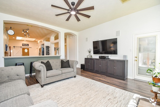 living area with arched walkways, ceiling fan, baseboards, and wood finished floors