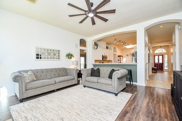 living area with baseboards, arched walkways, dark wood-style flooring, and ceiling fan with notable chandelier