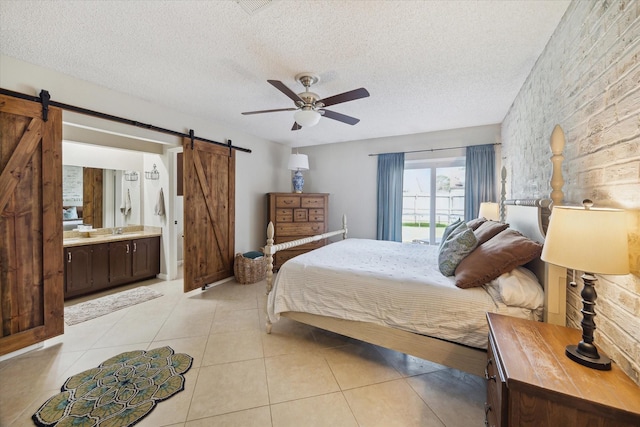 bedroom with a textured ceiling, a barn door, light tile patterned flooring, and a ceiling fan