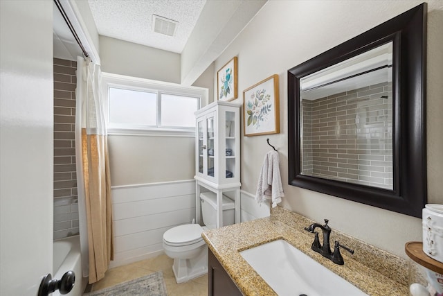 bathroom with a wainscoted wall, visible vents, toilet, a textured ceiling, and tile patterned flooring