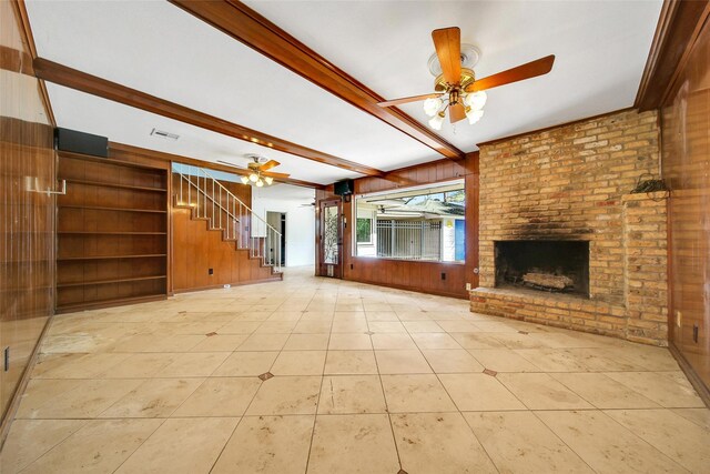 unfurnished living room with a fireplace, ceiling fan, stairs, wood walls, and beamed ceiling