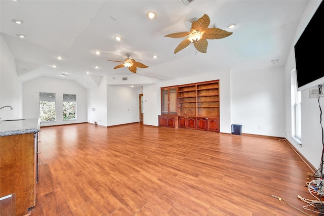 unfurnished living room featuring a sink, light wood-style flooring, ceiling fan, and vaulted ceiling