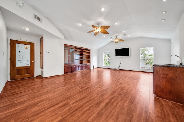 unfurnished living room with wood finished floors, baseboards, visible vents, a sink, and vaulted ceiling