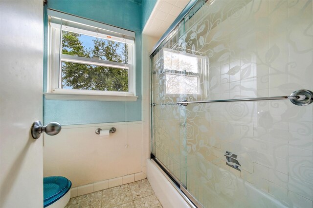 bathroom featuring bath / shower combo with glass door, tile patterned flooring, and toilet