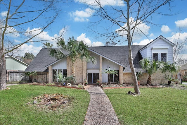 mid-century home featuring brick siding, fence, a front lawn, and roof with shingles