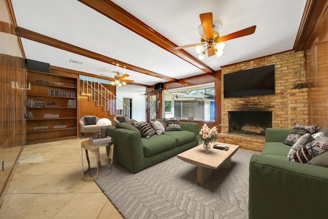 living room featuring beamed ceiling, stairway, wood walls, a brick fireplace, and ceiling fan