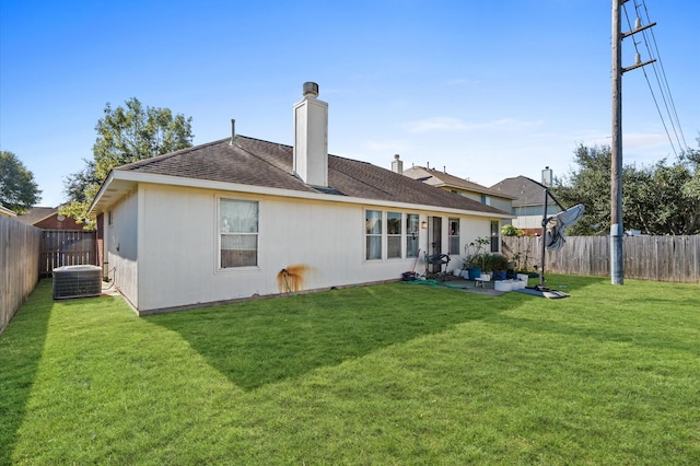 rear view of house with a chimney, a fenced backyard, a shingled roof, central AC unit, and a yard