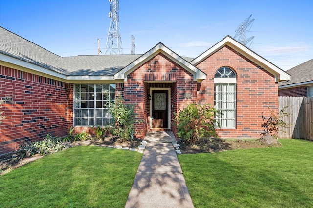 view of front facade featuring brick siding, a front yard, fence, and a shingled roof