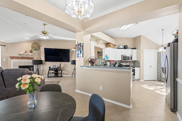 dining area featuring light tile patterned floors, ceiling fan with notable chandelier, vaulted ceiling, and a tile fireplace