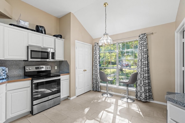 kitchen featuring dark countertops, vaulted ceiling, stainless steel appliances, white cabinetry, and backsplash