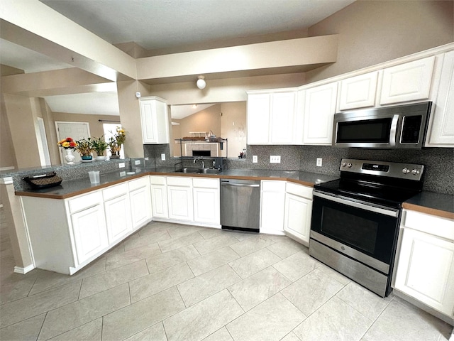 kitchen with white cabinetry, tasteful backsplash, a sink, dark countertops, and appliances with stainless steel finishes
