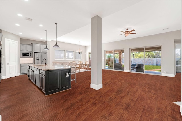 kitchen featuring dark wood-style floors, appliances with stainless steel finishes, open floor plan, a kitchen island with sink, and a sink