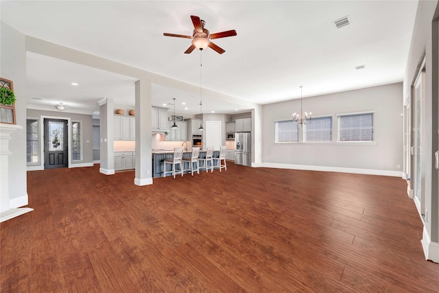 unfurnished living room featuring dark wood-style flooring, a fireplace, visible vents, baseboards, and ceiling fan with notable chandelier