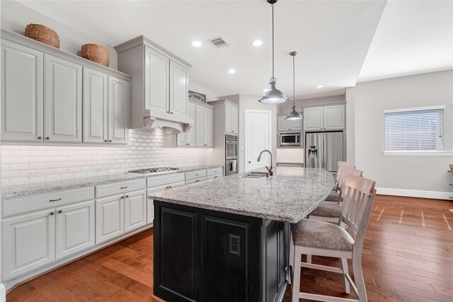 kitchen with wood finished floors, a sink, visible vents, appliances with stainless steel finishes, and decorative backsplash