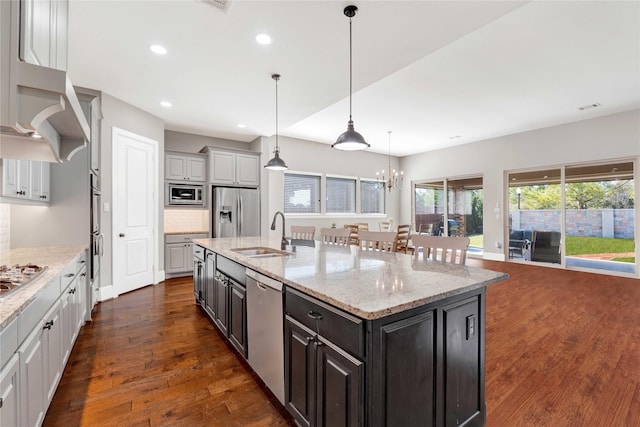 kitchen with dark wood finished floors, stainless steel appliances, decorative backsplash, a kitchen island with sink, and a sink