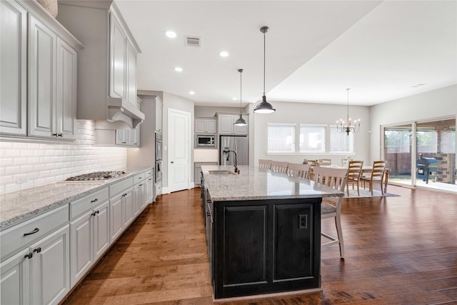 kitchen with dark wood-style floors, appliances with stainless steel finishes, a kitchen breakfast bar, a sink, and backsplash