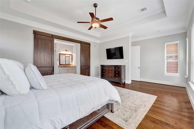 bedroom with a barn door, wood finished floors, visible vents, baseboards, and a tray ceiling