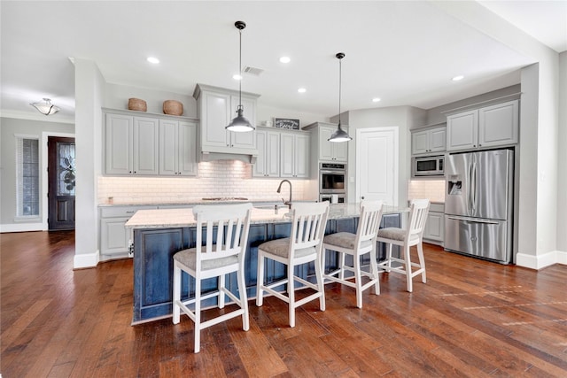 kitchen featuring dark wood-type flooring, a sink, baseboards, appliances with stainless steel finishes, and a center island with sink