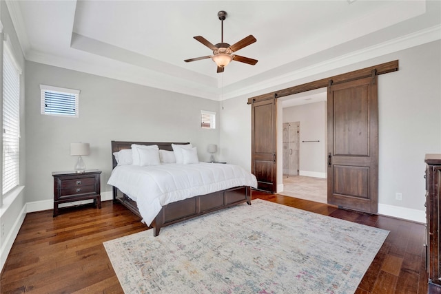 bedroom with a barn door, baseboards, a raised ceiling, and dark wood-type flooring